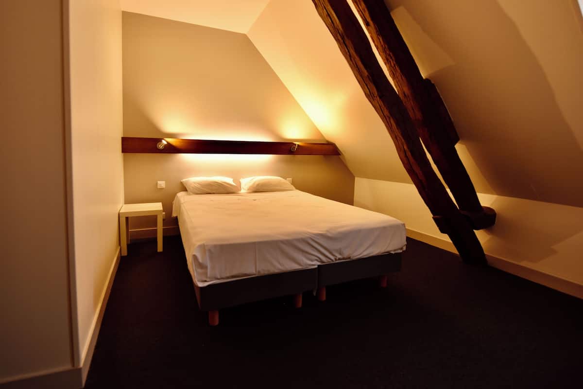 A bedroom with a bed, bedside table, and a sloped ceiling.