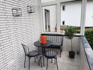En balkon med en murstensvæg, et rundt bord med fire stole, en lille orange kurv og en potteplante.