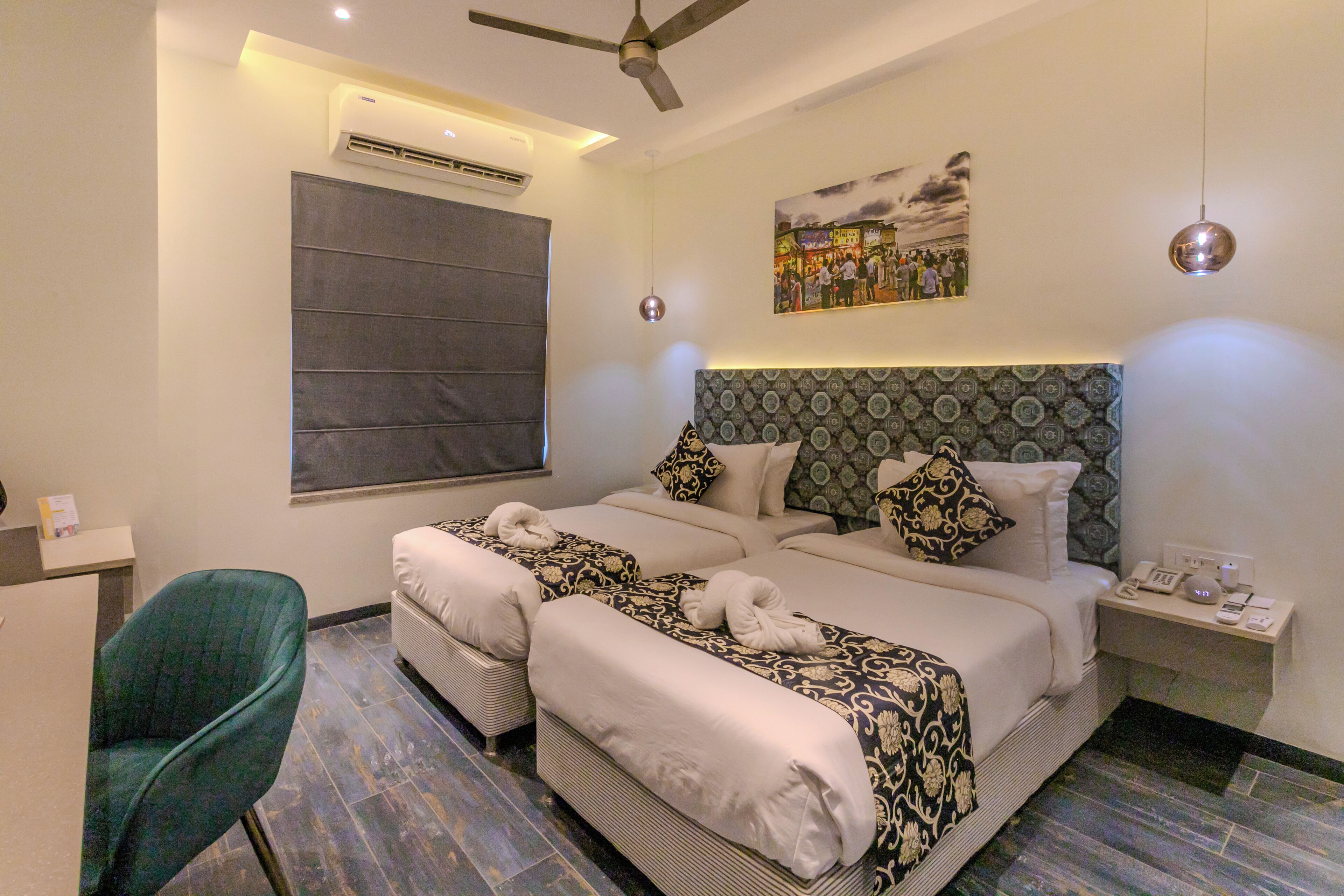 A hotel room with two beds, a desk, a chair, a ceiling fan, and a wall-mounted air conditioner.