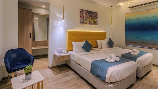 A hotel room with a large bed, a small desk, a chair, and a large window. - World Inn (Visakhapatnam)