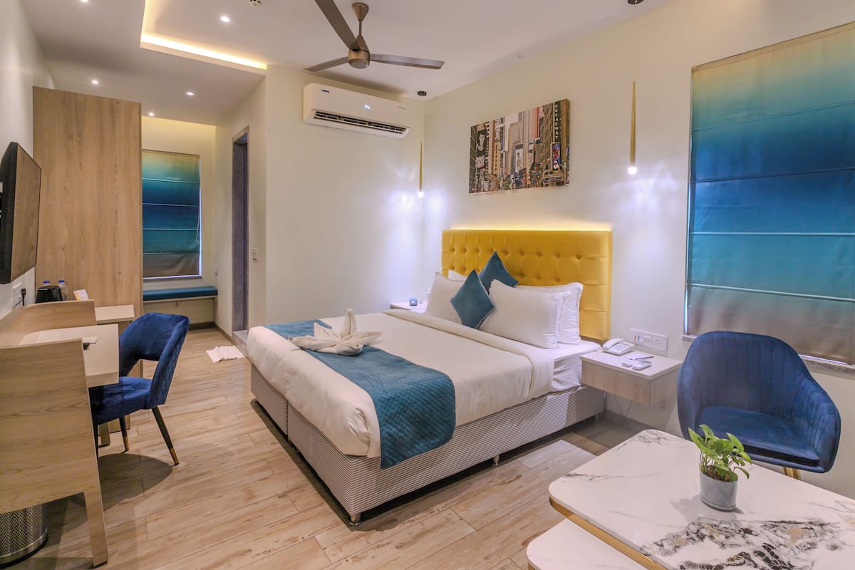 Une chambre d’hôtel moderne équipée d’un lit, d’un bureau, d’une chaise, d’une petite table avec une plante et d’un ventilateur de plafond.
