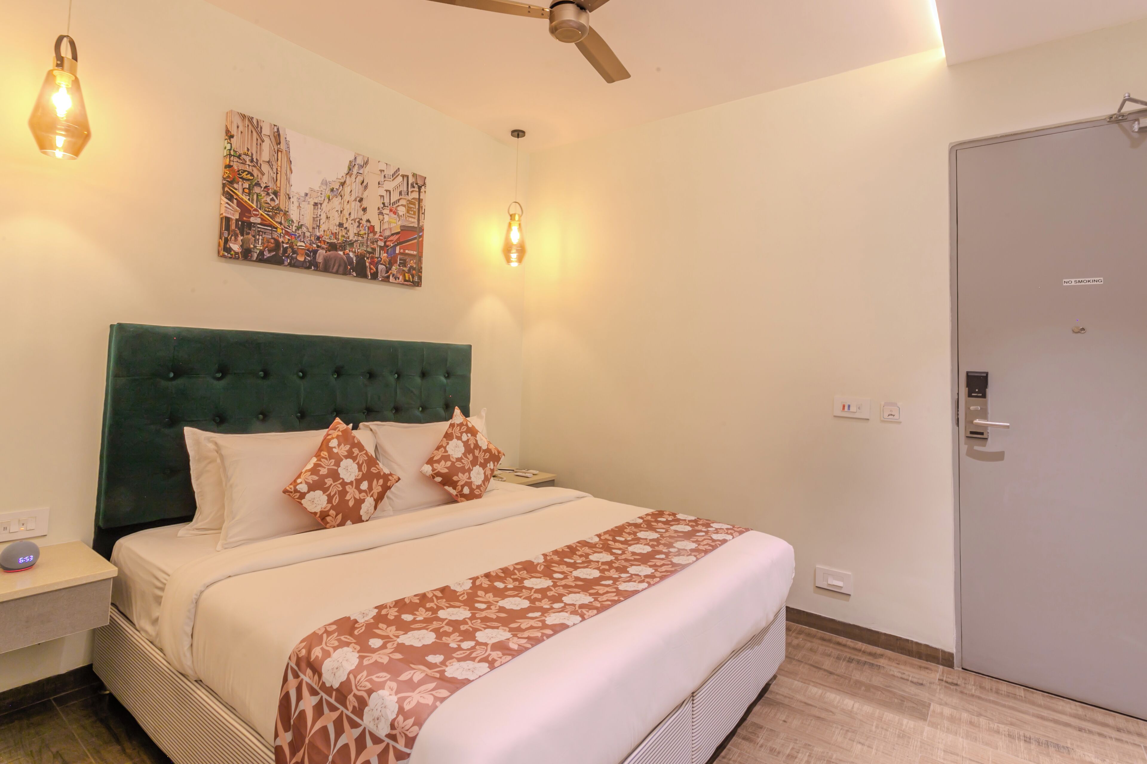 Habitación de hotel con una cama grande, un ventilador de techo, una obra de arte colgada en la pared y una puerta con un cartel de 'No Smoking'.