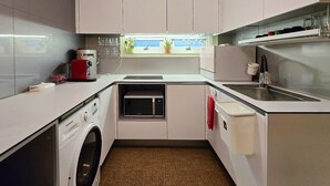 Una cuina compacta amb armaris blancs, un microones integrat, una cafetera i una rentadora.