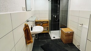 Une salle de bain moderne avec une douche à l’italienne en verre, un lavabo blanc et un tapis noir sur le sol.