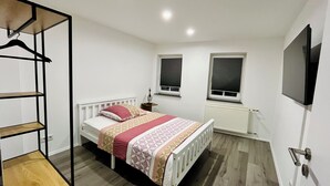 Une chambre à coucher comprenant un lit, une armoire, un radiateur et deux fenêtres.