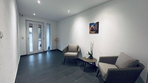 Un hall d’entrée spacieux, avec deux fauteuils en osier, une petite table et un vase de fleurs.