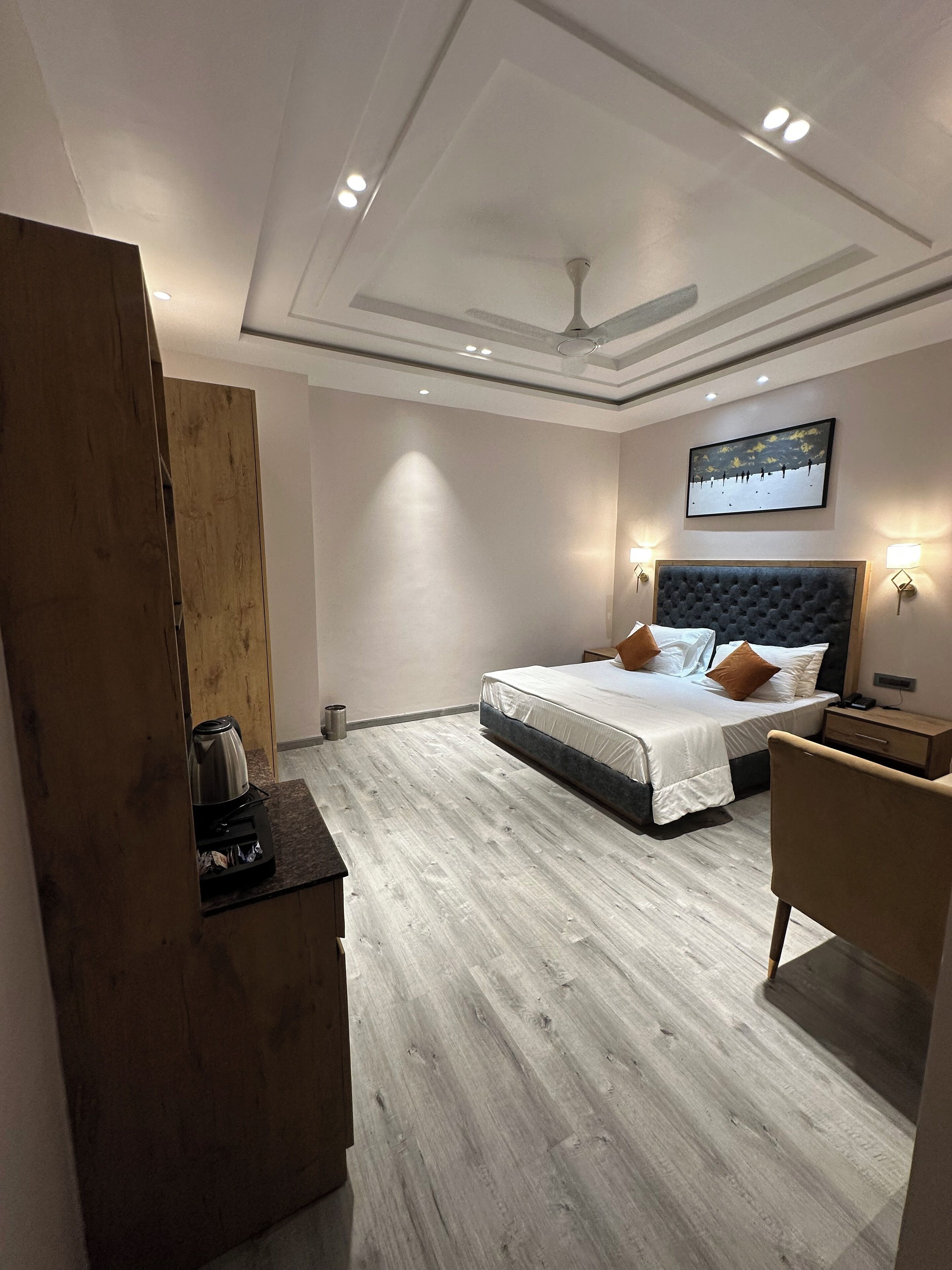 Een moderne hotelkamer met een groot bed, een houten bureau, een plafondventilator en een schilderij aan de muur.