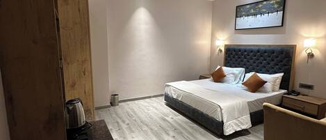 A modern hotel room with a large bed, a wooden desk, a ceiling fan, and a painting on the wall.