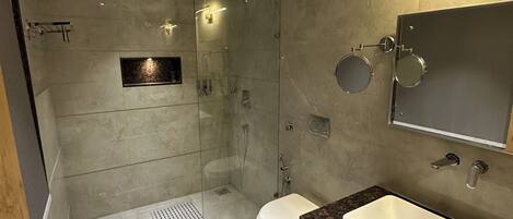 Un baño moderno con cabina de ducha de vidrio, inodoro blanco y tocador con lavamanos.