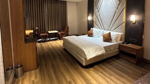 Une chambre moderne avec un grand lit, un coin salon avec des fauteuils et un bureau en bois.