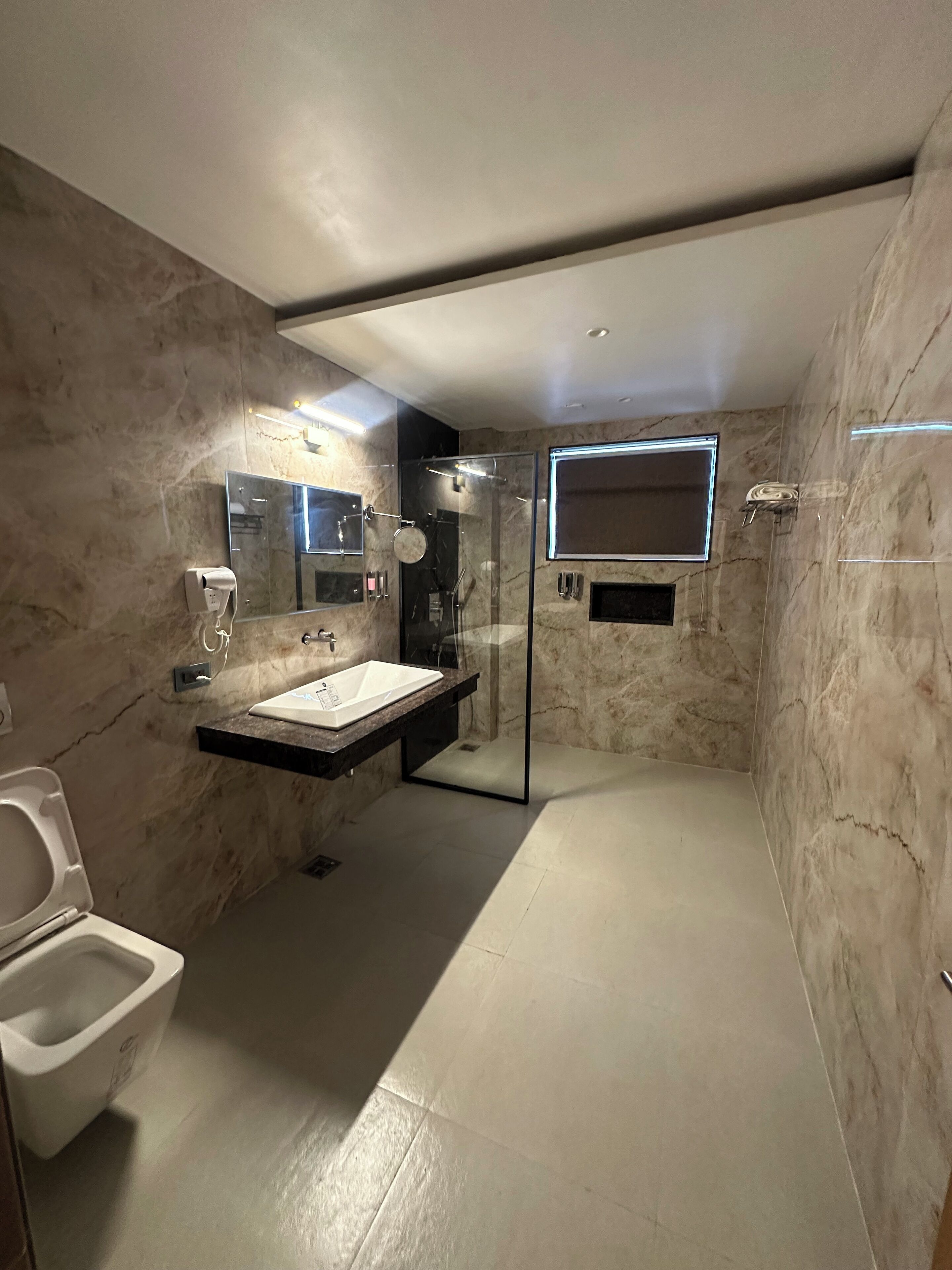 A modern bathroom with a marble wall, a glass-enclosed shower, a white sink, and a toilet.