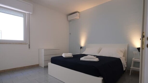 Ein Schlafzimmer mit Bett, Nachttischen, einem Fenster und einer Klimaanlage.