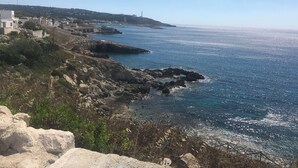 Eine Küstenlandschaft mit felsigem Gelände, blauem Meer und einem fernen Leuchtturm.