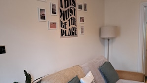 Een gezellige woonkamer met een bank, een aan de muur bevestigd fotolijstje, en een kleine tafel met een plant.