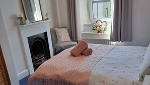 Een slaapkamer met een bed, een stoel, een open haard, een raam met gordijnen en uitzicht op de omgeving.