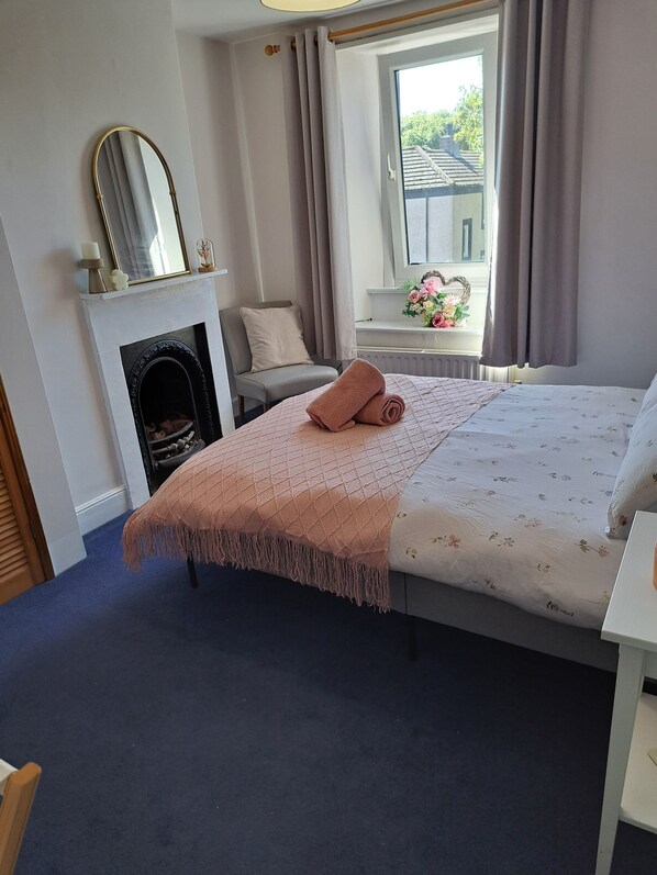 Une chambre à coucher comprenant un lit, une chaise, une cheminée, une fenêtre avec des rideaux et une vue sur l’extérieur.