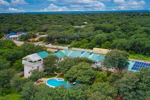 A residential area with a large house featuring a swimming pool, surrounded by dense greenery and a clear view of the ocean.