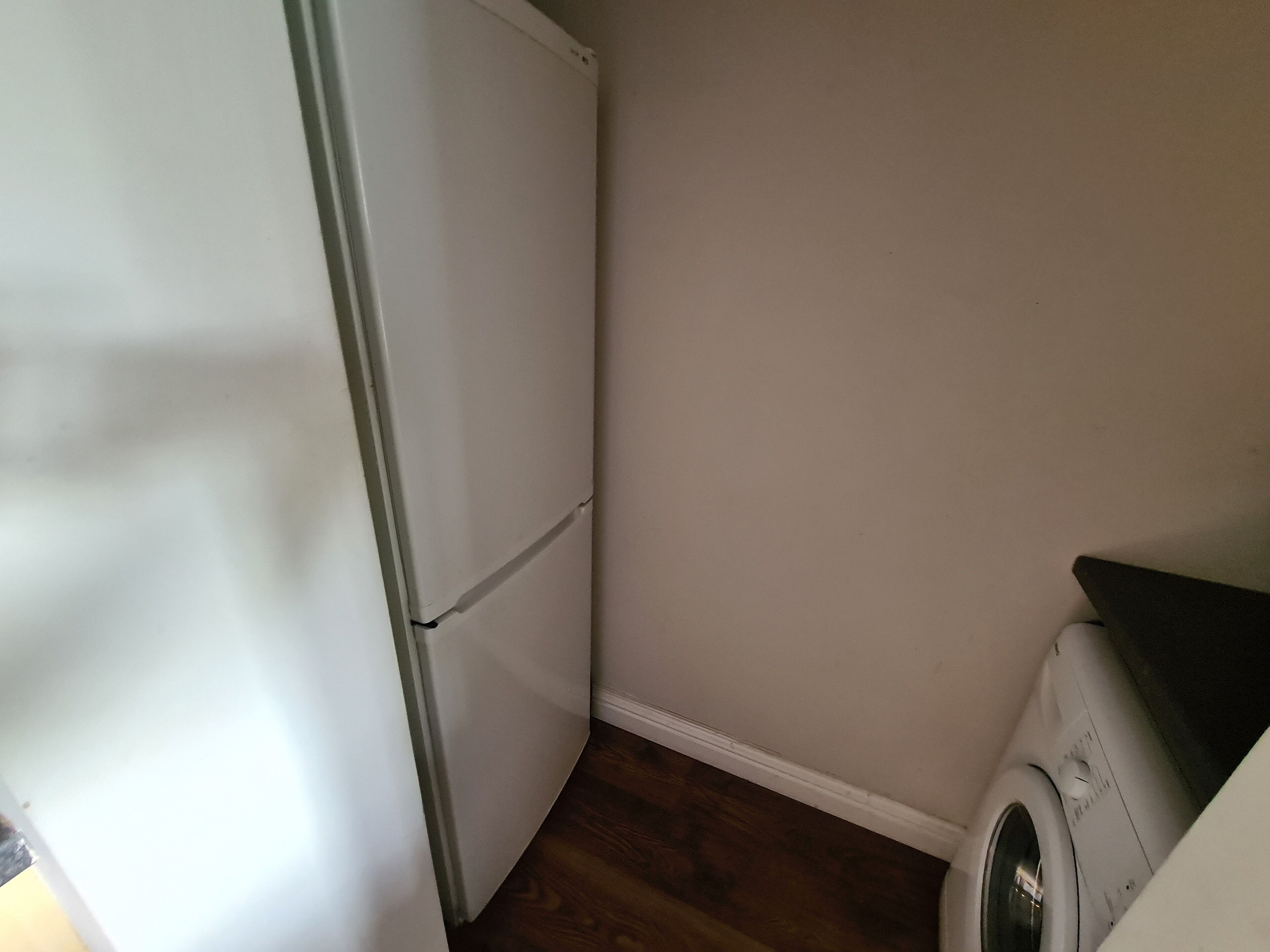 Een kleine wasruimte met een wasmachine en een witte koelkast.