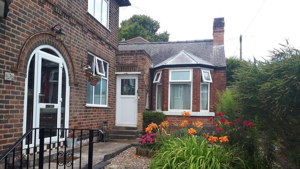 A brick house with a white door and windows, surrounded by a garden with various plants and flowers. - Cozy Nottingham Apartment With Perfect Location (Nottingham)