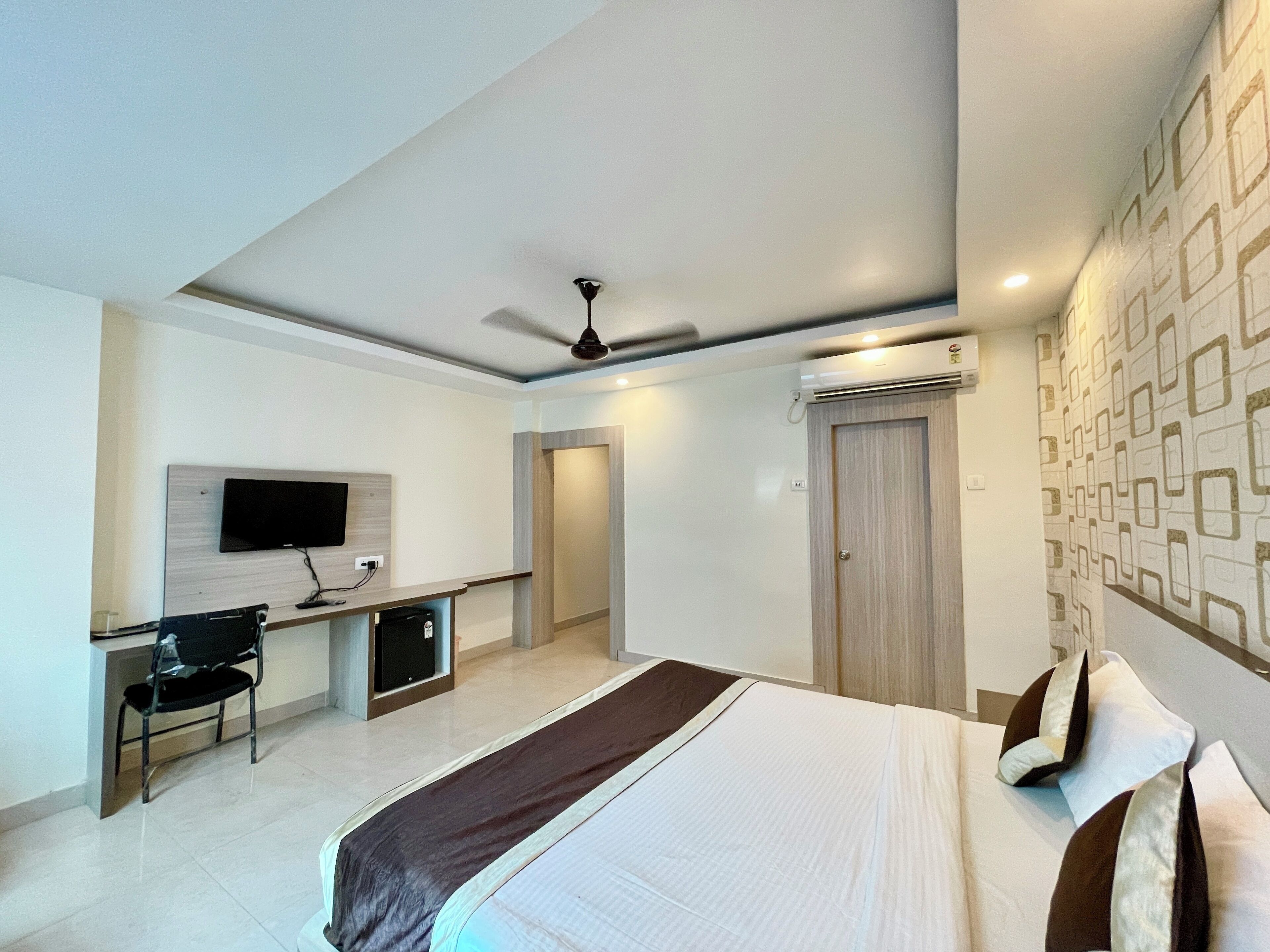 Una habitación de hotel moderna con una cama, un escritorio con una silla, un televisor y un ventilador de techo.