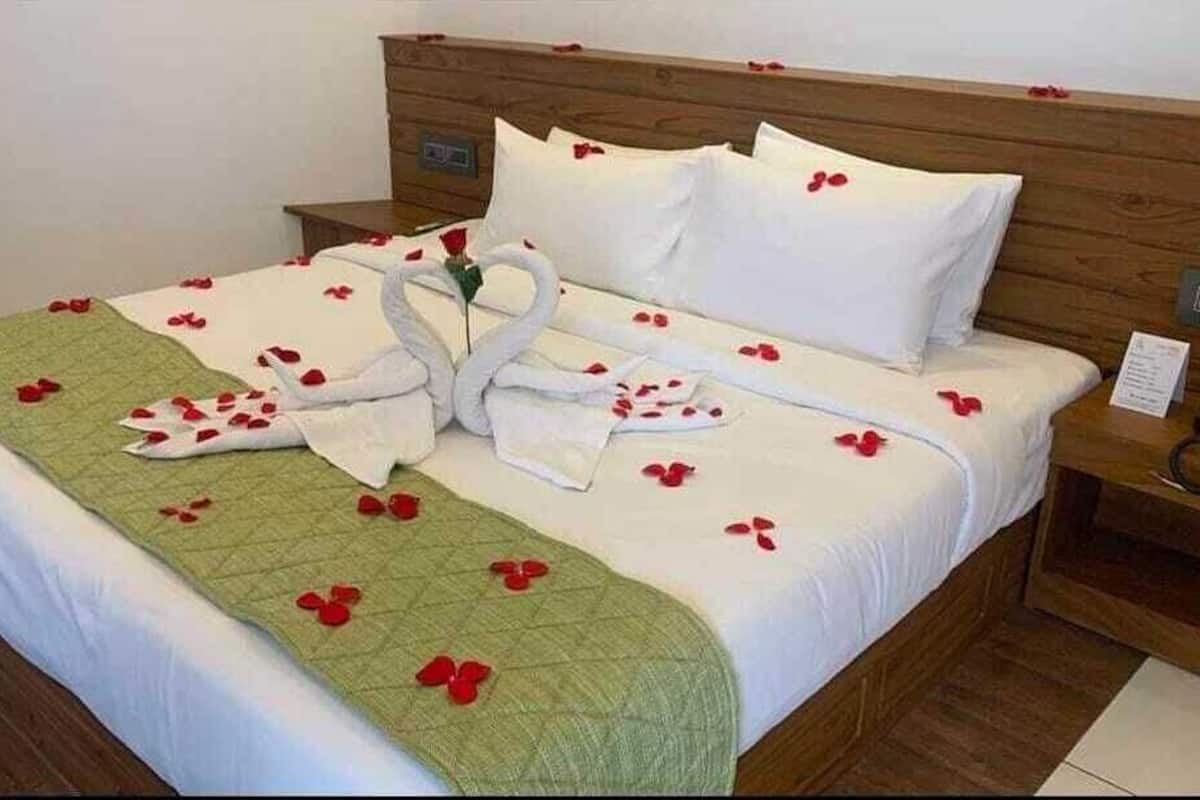 Un lit parfaitement fait, décoré de pétales de rose et orné de deux cygnes réalisés avec des serviettes, une couverture verte et du linge de lit blanc.