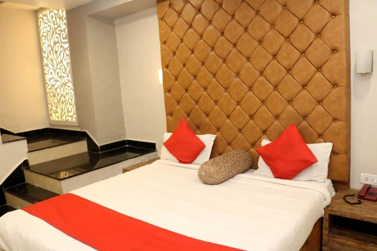 Een hotelkamer met een gestoffeerd hoofdeinde, een bed met witte beddengoed en rode kussens, een nachtkastje van hout met een telefoon en een decoratief paneel aan de muur.