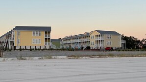 A beachfront hotel with multiple-story buildings, balconies, and a sandy beach in the foreground.