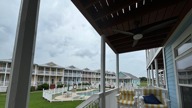 A covered outdoor area with a pool, white railings, and a view of multi-story buildings in the background.