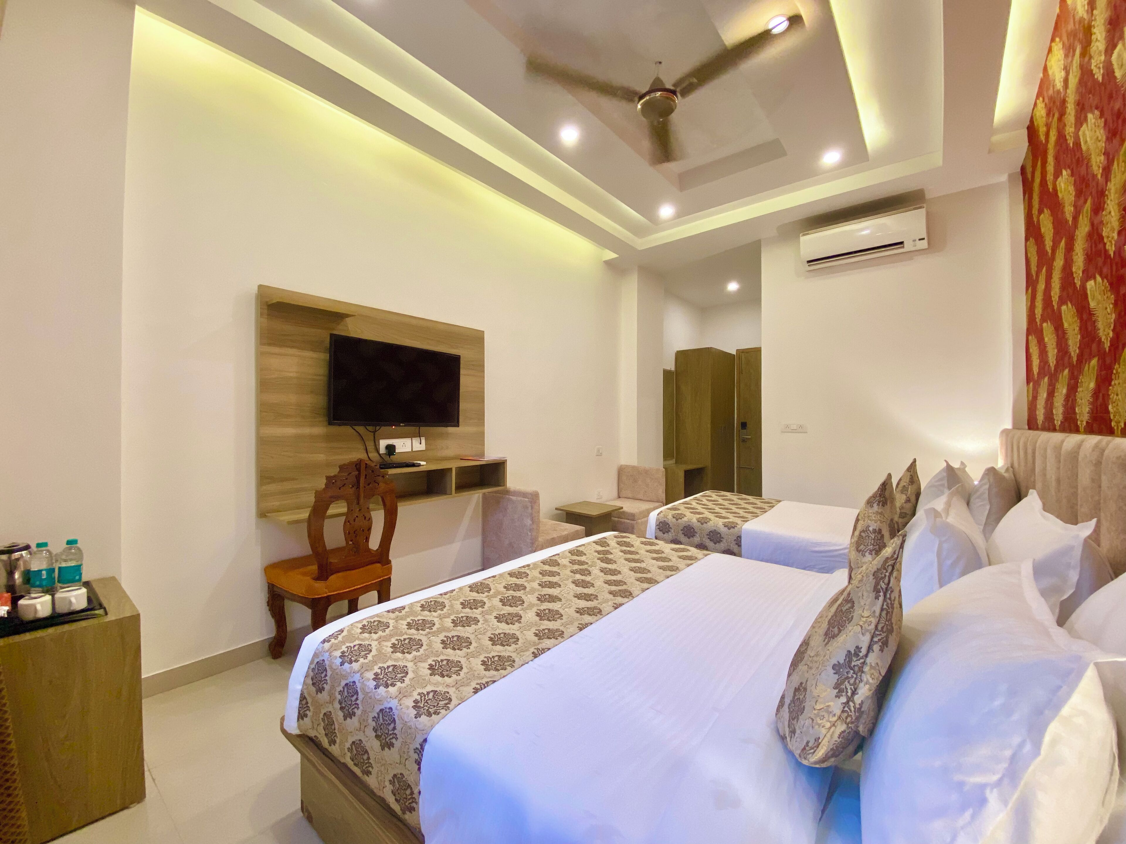 A hotel room with two beds, a TV mounted on the wall, a ceiling fan, and an air conditioning unit.