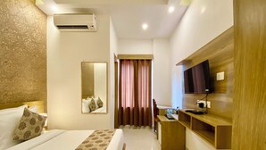 A hotel room with a bed, a TV, a desk, and a mirror. - Arogyadham Wellness Retreat (Rishikesh)