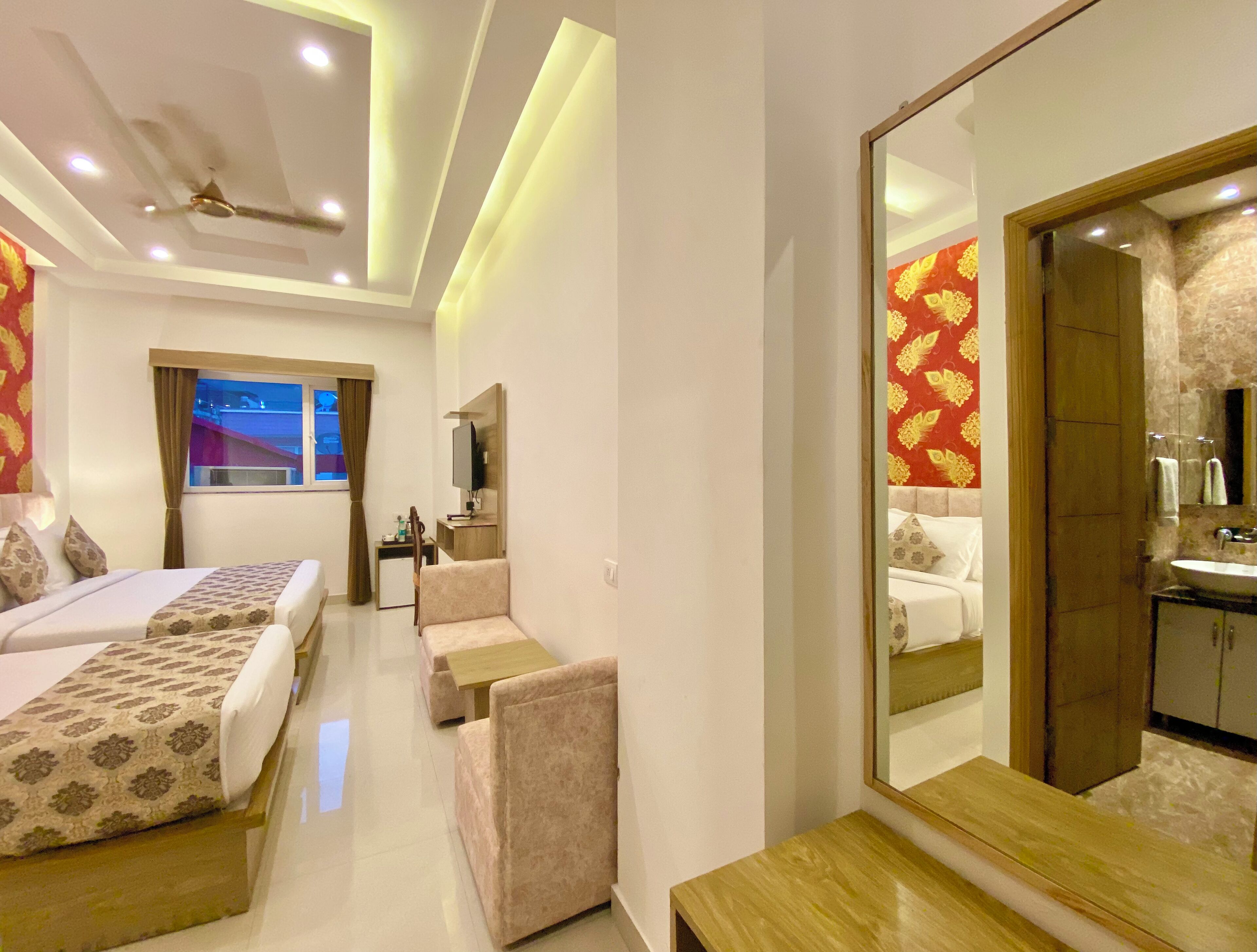 A hotel room with two beds, a desk, a chair, a TV, and a bathroom with a mirror and sink.