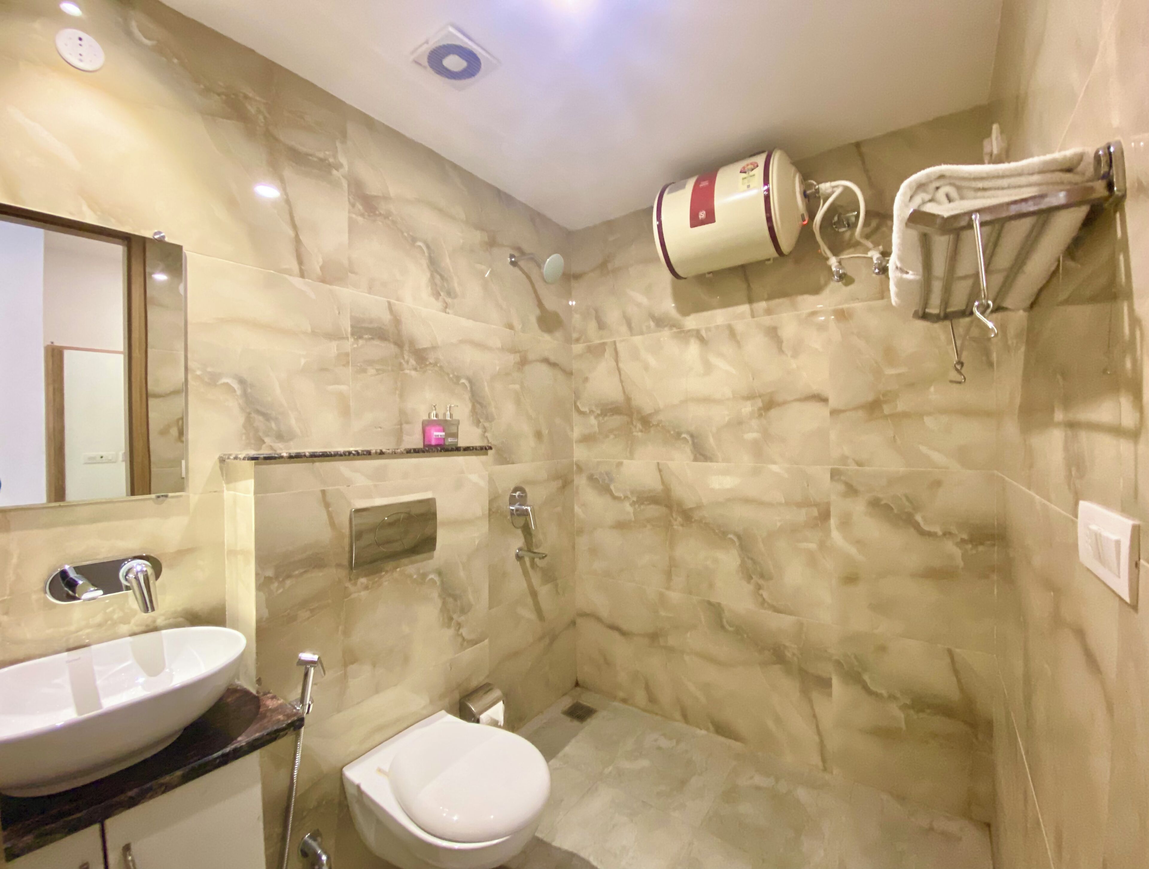 A bathroom with a marble wall, a sink, a toilet, a shower, and a towel rack.