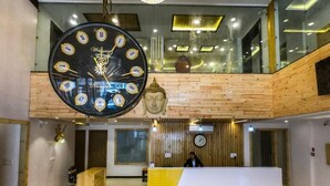 A hotel reception area with a large wall-mounted clock, a wooden reception desk, and a Buddha statue. - Arogyadham Wellness Retreat (Rishikesh)