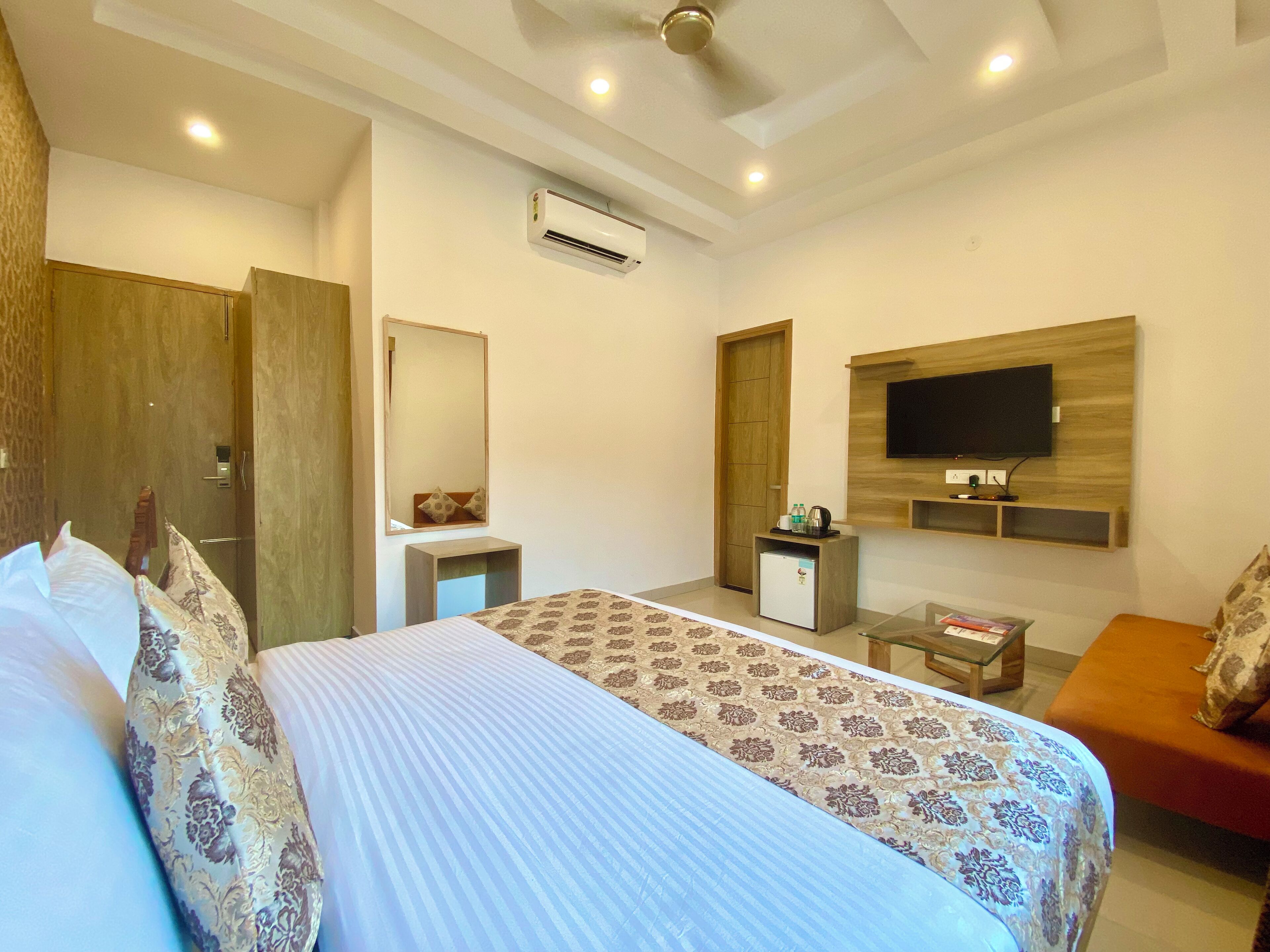 A hotel room with a large bed, a small desk, a TV mounted on the wall, and a ceiling fan.
