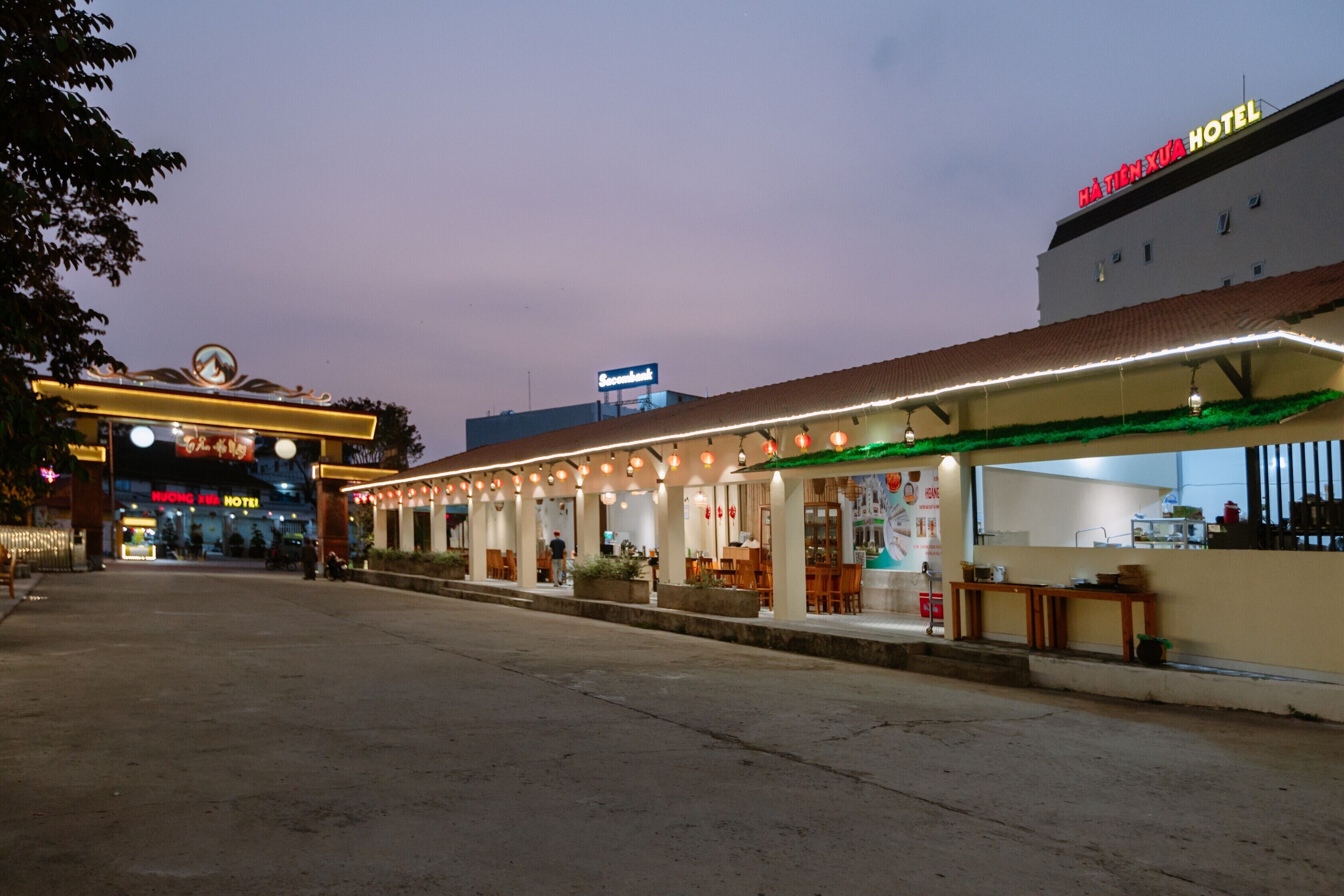 A hotel with a covered outdoor seating area, a visible restaurant, and a sign for the hotel.