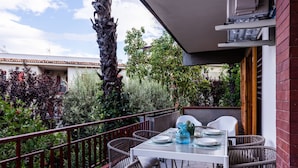 A balcony with a white table set for dining, wicker chairs, and a red railing.
