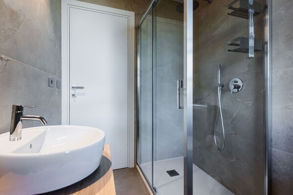 Un baño moderno con lavamanos blanco, cabina de ducha con mampara de vidrio y una puerta.