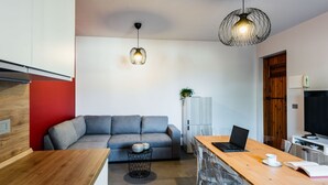 A modern kitchen with a wooden countertop, a grey sofa, and a dining area with a wooden table and chairs.
