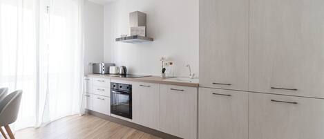 A modern kitchen with light wood cabinets, a built-in oven, and a stainless steel range hood.