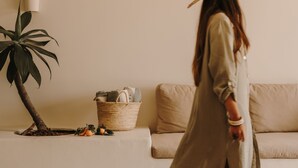 Eine Person geht durch einen Raum mit einem Sofa, einer Lampe und einer Pflanze.