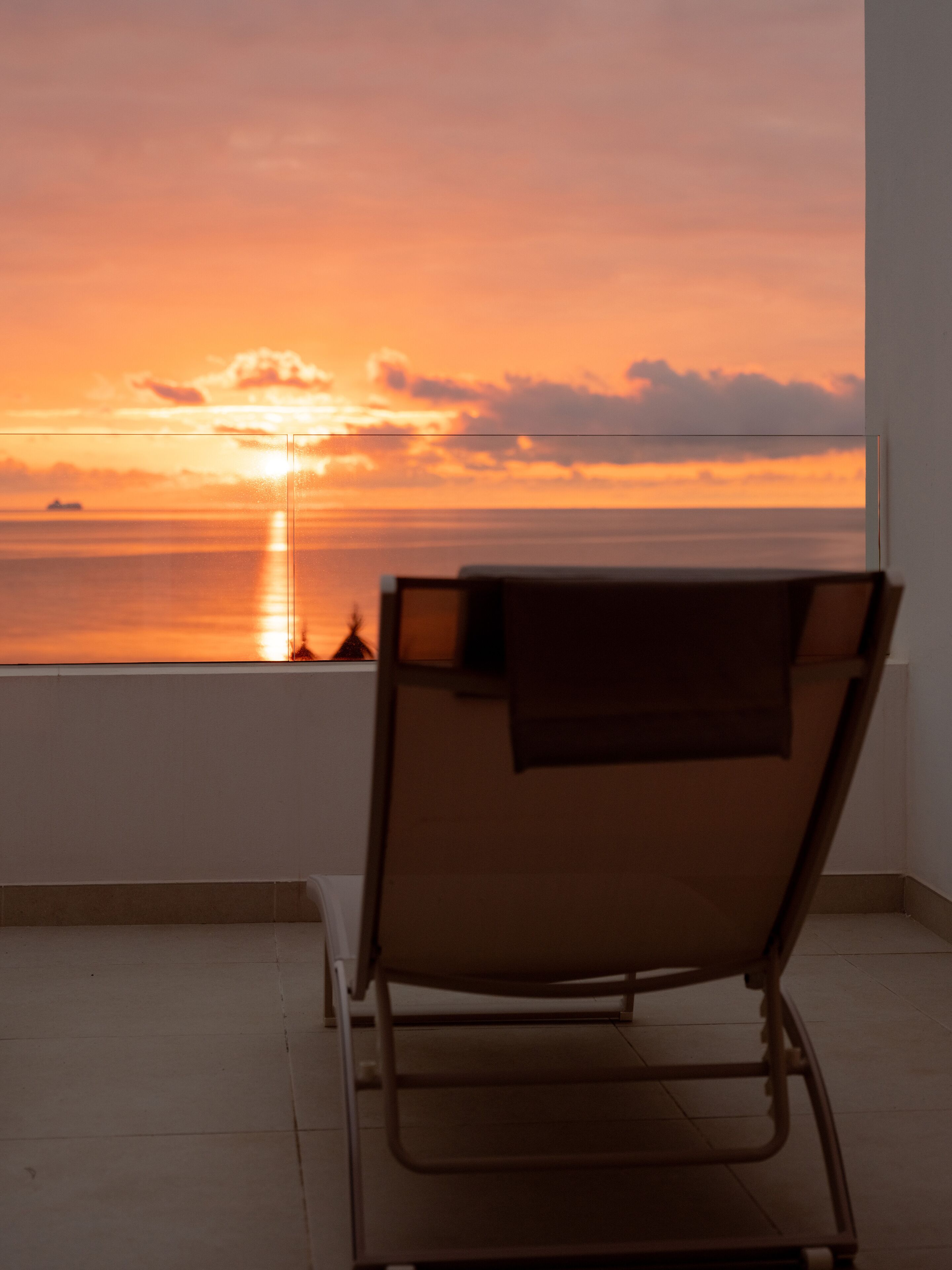 Una silla reclinable con vistas a la puesta de sol sobre el océano.