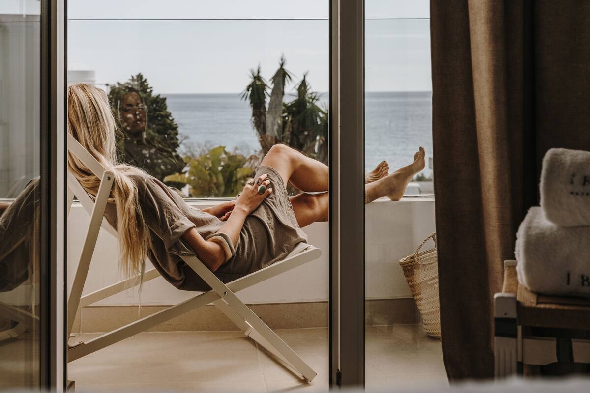 Eine Person entspannt in einem weißen Stuhl und genießt den Blick auf das Meer durch eine Glastür.