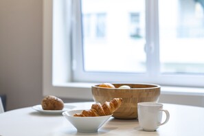Een ontbijtsetting met croissants, een mok en een houten kom op een tafel bij een raam.