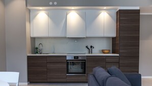A modern kitchen with built-in appliances, a dining area with a white table and chairs, and a dark-colored sofa in the foreground. - Forenom Serviced Apartments Bergen City (Bergen)