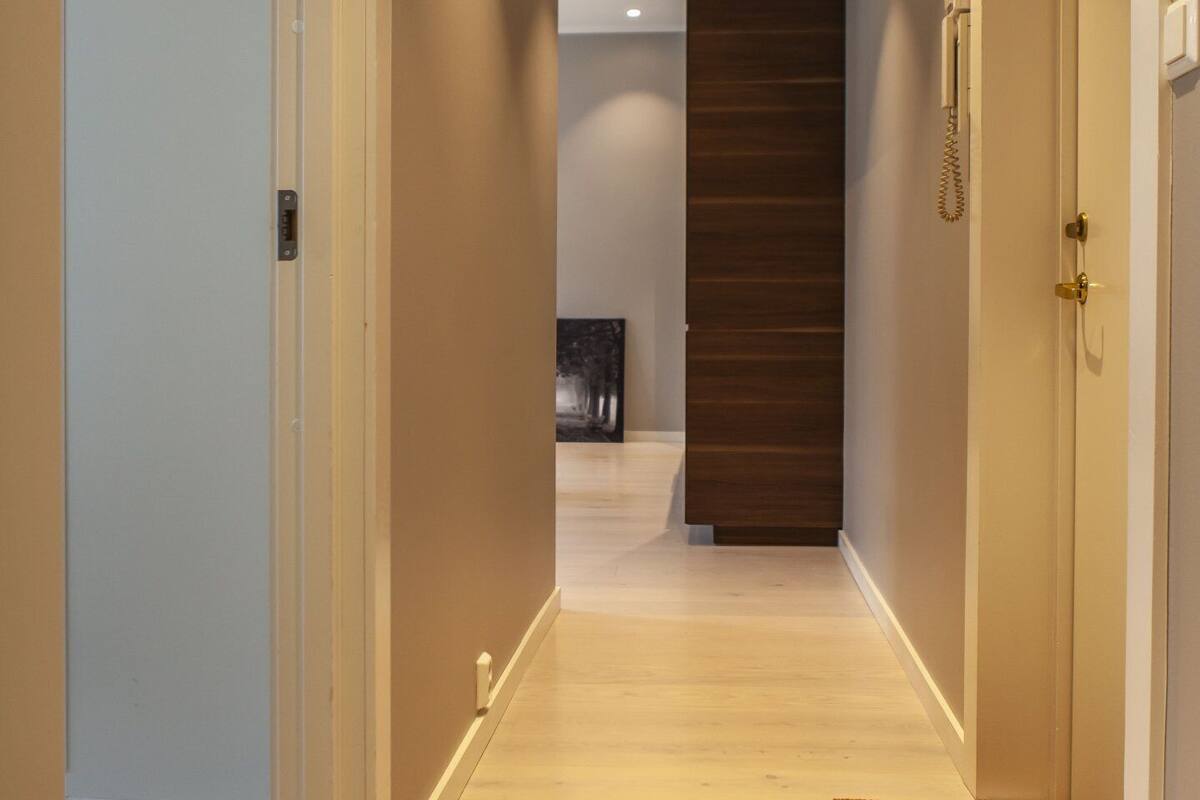 Un couloir avec une porte en bois, un paillasson et un plancher de couleur claire.