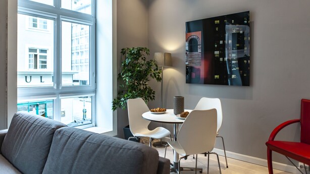 A modern living room with a grey sofa, a dining area with white chairs and a table, a potted plant, and a painting on the wall. - Forenom Serviced Apartments Bergen City (Bergen)
