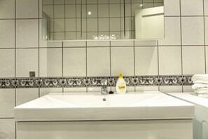 Een badkamer met een wit wastafel, een spiegel en een decoratieve tegelrand.