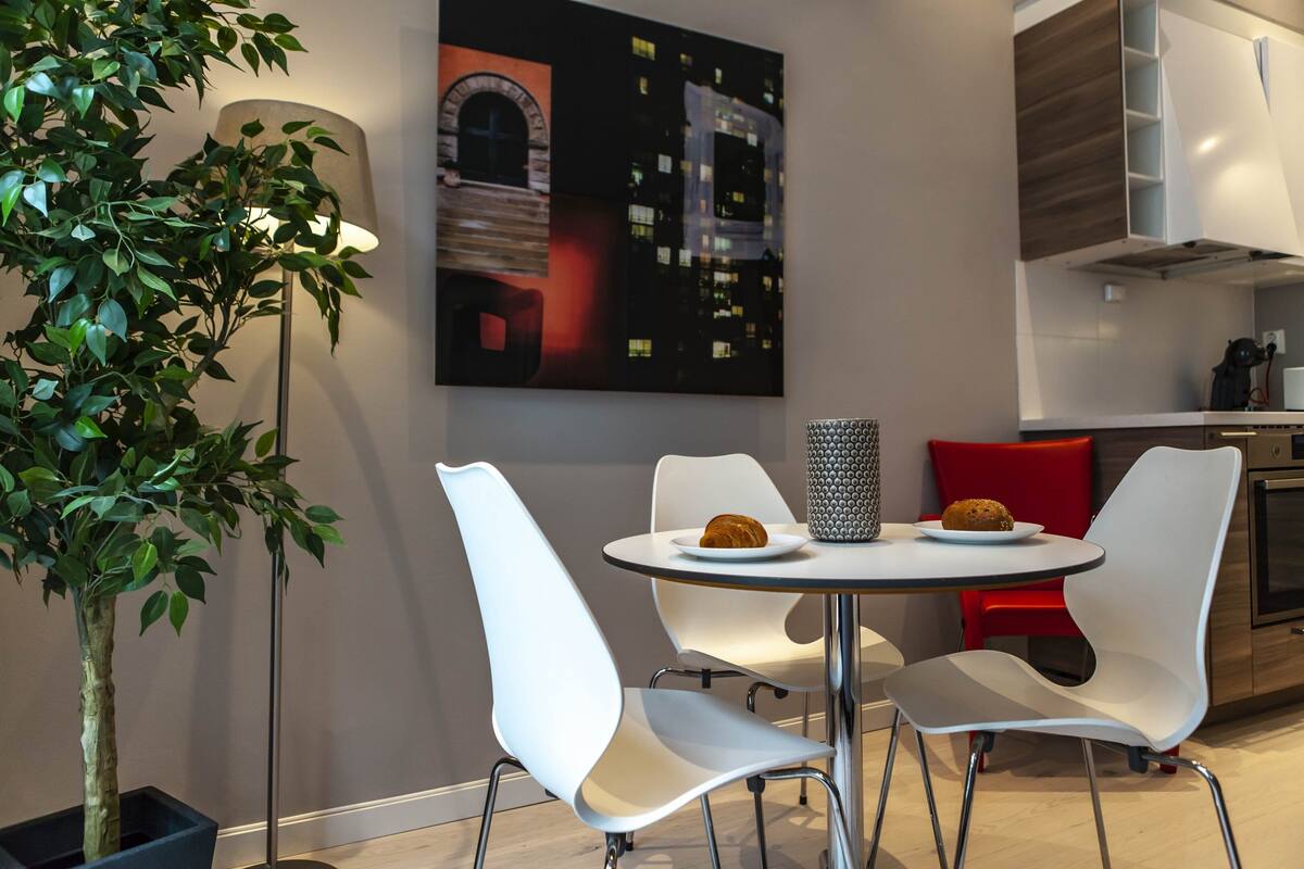 Une cuisine moderne avec des meubles blancs, une table à manger avec des chaises blanches et une plante en pot.