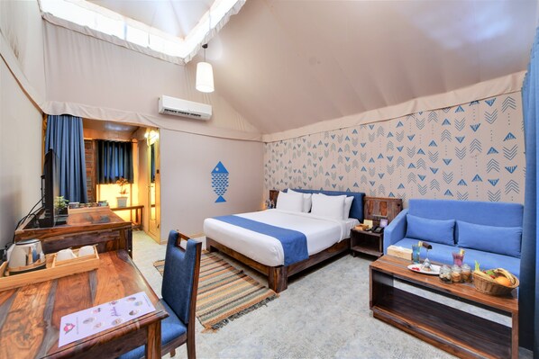 Habitación de hotel con cama, sofá, escritorio y silla. Se ve una ventana con cortinas, un aire acondicionado de pared y una pared con diseño.