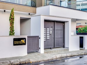 A modern building with a grey entrance, a sign reading "Premier Downtown Residence," and a small garden with a tall plant. - Sanders Premier Downtown - Full Building (Limassol)